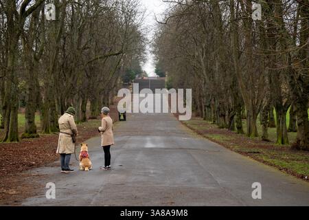 Una giovane coppia passeggia lì con il cane attraverso Queens Park, Govanhill, Glasgow, Scozia. Foto Stock
