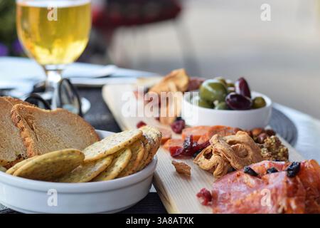 Tagliere di salumi con salumi e frutta secca, olive e cracker su un tavolo del ristorante nel patio Foto Stock
