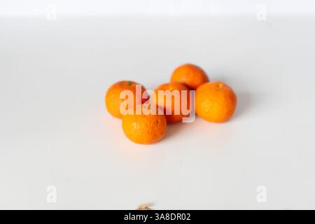 Un gruppo di arance mandarine fresche e luminose disposte su una superficie bianca pulita. Questi succosi agrumi sono uno spuntino delizioso e salutare, perfetto per Foto Stock