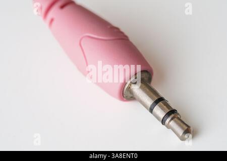Primo piano di un jack audio rosa da 3,5 mm su sfondo bianco, con spina in metallo e involucro in plastica per i collegamenti audio. Foto Stock
