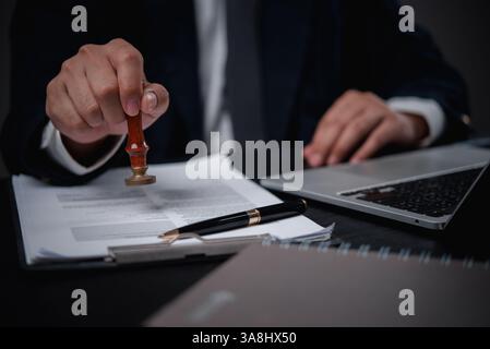 l'uomo in un ufficio timbra un documento ufficiale con un sigillo di gomma, che simboleggia l'autorità e l'approvazione nell'elaborazione di documenti legali come gli accordi o Foto Stock