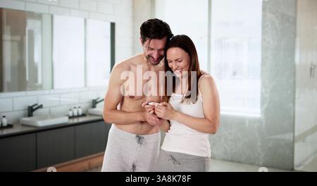 Coppia eccitata che celebra il test di gravidanza positivo in una scena accogliente del bagno. Potenziali professioni: Ostetrico, ginecologo, consulente matrimoniale, fa Foto Stock