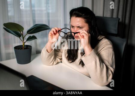 Una donna d'affari in un ufficio domestico si sente frustrata e si concentra sul lavoro. Donna in occhiali da vista che lavora al computer gestendo il processo di lavoro mentre è seduta Foto Stock