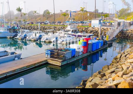 Oceanside, California - 3 gennaio 2025: Tranquillo porto di Oceanside, California, con barche da pesca e vivaci cestini per la spazzatura sotto la soffice mattinata Foto Stock
