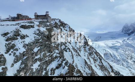 Volo aereo con una rotazione completa intorno al Gornergrat invernale con vista del Cervino, della stazione ferroviaria di Gornergrat e dell'hotel, del ghiacciaio Gorner e del Monte Rosa. Foto Stock