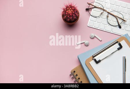Forniture per ufficio e dispositivi tecnologici disposti in modo ordinato su un desktop rosa, creando uno spazio di lavoro ideale per la produttività e la concentrazione Foto Stock