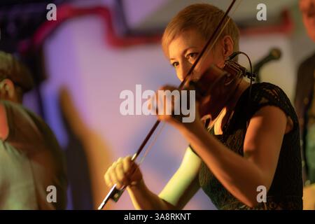 Una violinista femminile suona il violino. La band si esibisce sul palco, concerto di musica rock. Foto Stock