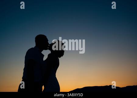 Sagome di sposa e sposo baciati sullo sfondo di un tramonto sulle montagne Foto Stock