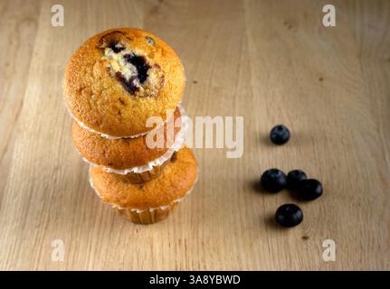 Tre muffin impilati uno sopra l'altro con mirtilli sul fondo. I muffin sono ricoperti di mirtilli e sono seduti su un tavolo di legno Foto Stock