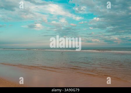 Onde dolci si infrangono contro la riva sotto un cielo luminoso e nuvoloso. Foto Stock
