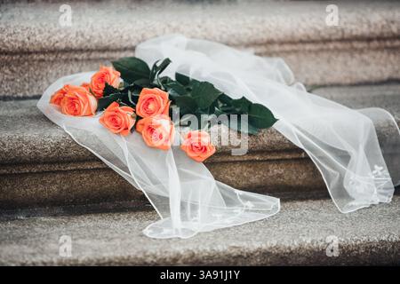 Un bouquet di rose arancioni si trova su un panno bianco su una scala. Le rose sono disposte in modo che non si tocchino l'un l'altro, e il panno lo è Foto Stock