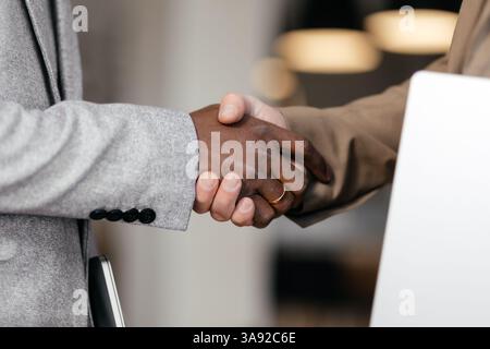 Primo piano due uomini d'affari di nazionalità diverse che stringono la mano. Mani bianche e nere insieme. Accordo di cooperazione, gesto di benvenuto Foto Stock