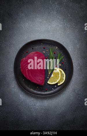 Filetto di tonno rosso fresco, per bistecche, crude, vista dall'alto, su un piatto nero, nessuno Foto Stock
