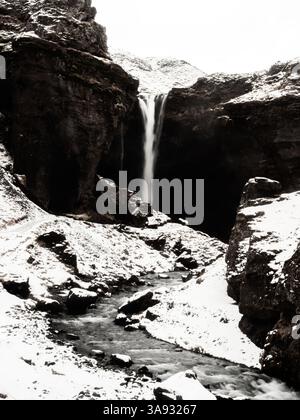 Cascata di Kvernufoss in inverno: Cascate di acqua ghiacciata tra rocce innevate che formano un ruscello panoramico. Natura islandese grezza nella sua forma più pura Foto Stock