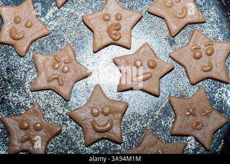 Un vassoio pieno di biscotti a forma di stella che mostra varie espressioni facciali giocose. I dolcetti sono realizzati con impasto, pronti per essere cotti o decorati Foto Stock