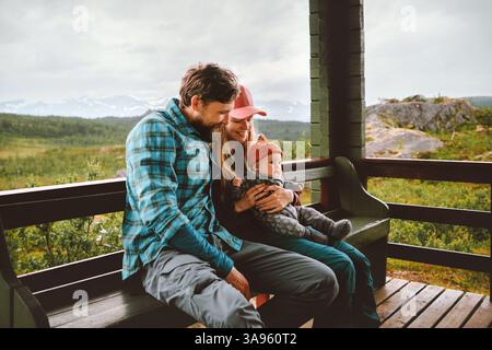 Vacanze in famiglia - padre e madre con bambino viaggiano insieme, genitori con bambini seduti sulla terrazza con vista sulle montagne emozioni felici e sincere bon Foto Stock