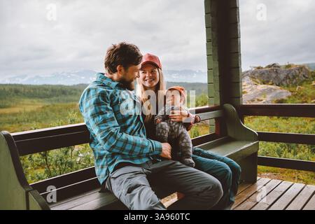 Stile di vita familiare padre e madre con neonati seduti in terrazza in viaggio in Norvegia, genitori con bambino felici emozioni schiette si uniscono insieme Foto Stock