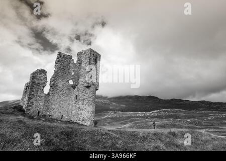 Spettacolare immagine in bianco e nero di un turista che guarda i grandi resti del castello di Ardvreck. Foto Stock