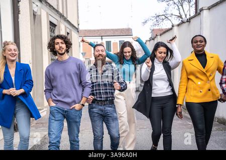 Gruppo di giovani adulti diversi che camminano e si divertono insieme in un ambiente urbano. Amici multiculturali che esprimono gioia ed energia nel casual fashio Foto Stock