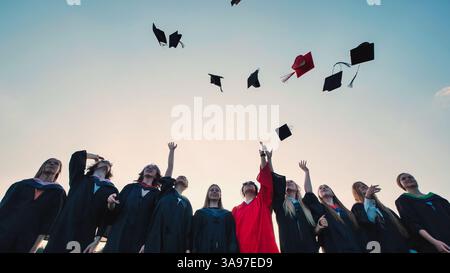 Gli allegri laureati celebrano il loro successo lanciando i loro berretti in aria con uno sfondo mozzafiato al tramonto Foto Stock