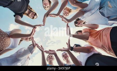 Gruppo di amici di scuola che si uniscono per mano formando una forma a stella, simboleggiando l'unità, il lavoro di squadra e l'amicizia, contro un cielo blu brillante Foto Stock