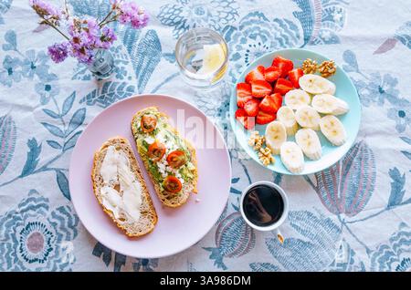 Una colazione ben organizzata con frutta fresca, pane tostato e caffè su una tovaglia floreale Foto Stock