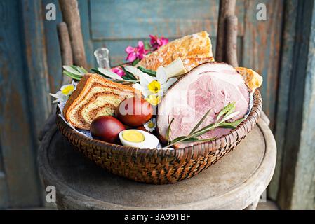 Cibo tradizionale pasquale con prosciutto, uova e pane nel cestino. Sfondo delle vacanze. Cestino pasquale pieno di prelibatezze di ogni genere Foto Stock