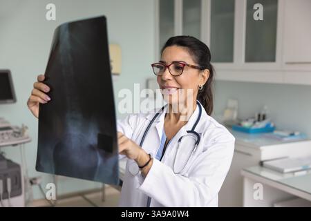 Traumatologia senior positiva medico donna che esamina l'immagine di scansione rm Foto Stock