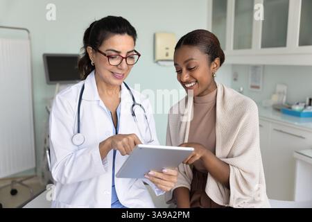 Allegro giovane paziente nero e donna medica matura che usa la compressa Foto Stock