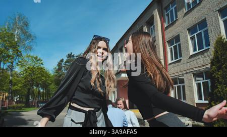 Due studenti gioiosi si impegnano in una vivace discussione fuori dalla scuola in una giornata di sole, scambiando risate ed entusiasmo Foto Stock