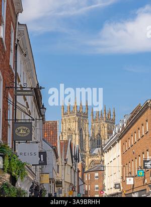 Storica strada della città fiancheggiata da negozi e torri di una cattedrale che si innalzano sopra i tetti. Un cielo con nuvole è sopra. Foto Stock