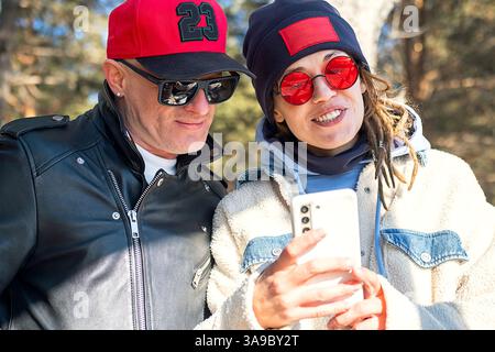 Donna con Dreadlock che scatta selfie con smartphone e uomo che indossa una giacca in pelle all'aperto. Foto Stock