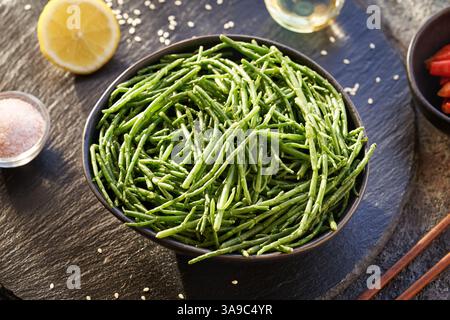 Una ciotola di alghe verdi fresche di Salicornia con limone, semi di sesamo, peperoncino e sale Foto Stock