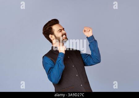 Concetto di successo. Eccitato ragazzo indiano sentirsi vittorioso e gesturing si su sfondo lilla Foto Stock