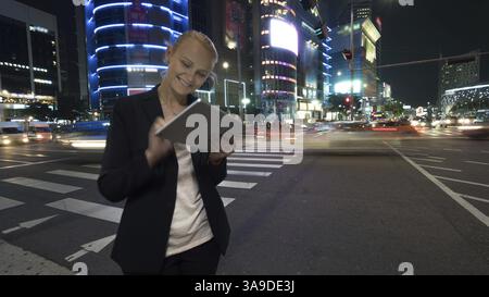 Giovane donna usando il touch pad sulla trafficata strada di notte Seoul città nella Repubblica di Corea. Edifici illuminati, autostrada con traffico automobilistico e pedestri Foto Stock