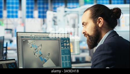 Il tecnico di fabbrica del fotovoltaico regola i parametri del sistema sul computer portatile per massimizzare la generazione di energia dalle celle solari. Uomo che utilizza un notebook che ottimizza l'alimentazione di energia nello stabilimento di produzione di pannelli solari, fotocamera B. Foto Stock