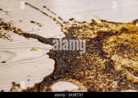 Spruzzo astratto di caffè liquido o salsa versato su una superficie di legno chiaro, creando un motivo organico e irregolare. Copia spazio Foto Stock