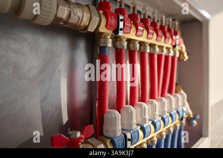 Collettore di riscaldamento sottopianale con valvole di controllo, flussometri e tubi rossi collegati. Sistema di riscaldamento domestico, impianto idraulico e controllo della temperatura Foto Stock