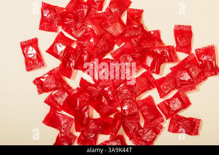 Caramelle rosse brillanti negli involucri sparsi su una superficie leggera, anche per la vista Foto Stock