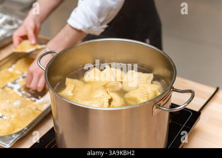 Uno chef prepara ravioli freschi fatti in casa bollendoli in una pentola di acciaio inossidabile su una stufa a induzione in una cucina professionale. Foto Stock