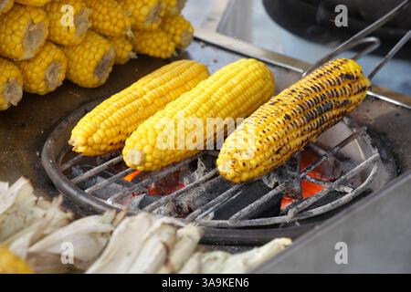 Pannocchie di mais grigliate su una griglia a carbone in un mercato estivo Foto Stock