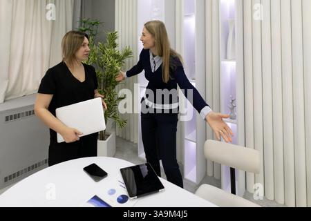 Due donne si impegnano in una vivace discussione in un ufficio moderno con arredamento bianco e verde, illustrando la collaborazione e il lavoro di squadra Foto Stock