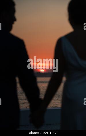 La coppia sagomata tiene le mani mentre guarda il tramonto sul wa Foto Stock