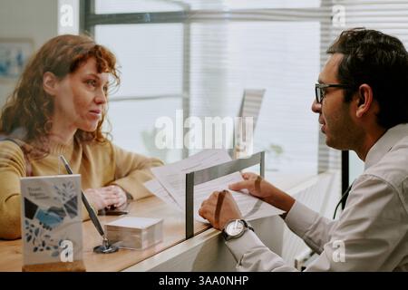 Ambiente di lavoro con due colleghi che discutono documenti all'interno della scrivania, donna con i capelli rossi e uomo con gli occhiali impegnato in conversazione Foto Stock