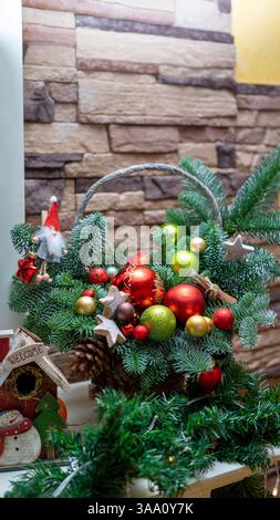 Cestino con la composizione di rami di albero di Natale per Capodanno, palle rosse, verdi e gialle e altre decorazioni per Capodanno. Immagine verticale. Foto Stock