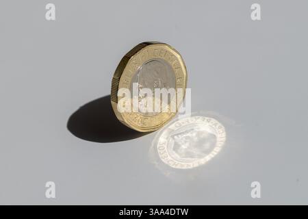 Una moneta inglese in libbre sul bordo con un'ombra e una riflessione luminosa audaci, che simboleggiano l'equilibrio, la ricchezza e la forza finanziaria nell'economia del Regno Unito Foto Stock