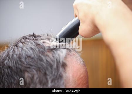 Primo piano di un uomo che rifinisce i capelli con un rasoio elettrico nel cortile posteriore Foto Stock