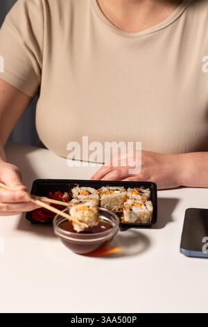 Donna che mangia sushi con bacchette a casa. Gustoso concetto di cucina asiatica. Panini di sushi in pacchetto da asporto. Concetto di consegna. Foto Stock