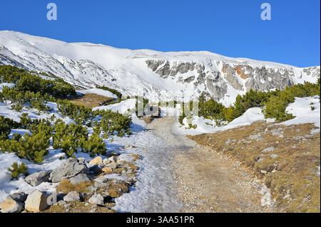 Catena montuosa panoramica innevata contro il vivace cielo blu. Soleggiato sentiero escursionistico con neve e campi di ghiaccio. Monte RAX, Alpi austriache. Foto Stock