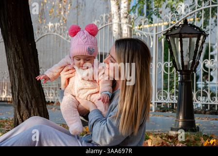 Mamma e bambino in caldi abiti autunnali che giocano all'aperto in un parco alberato. Foto Stock